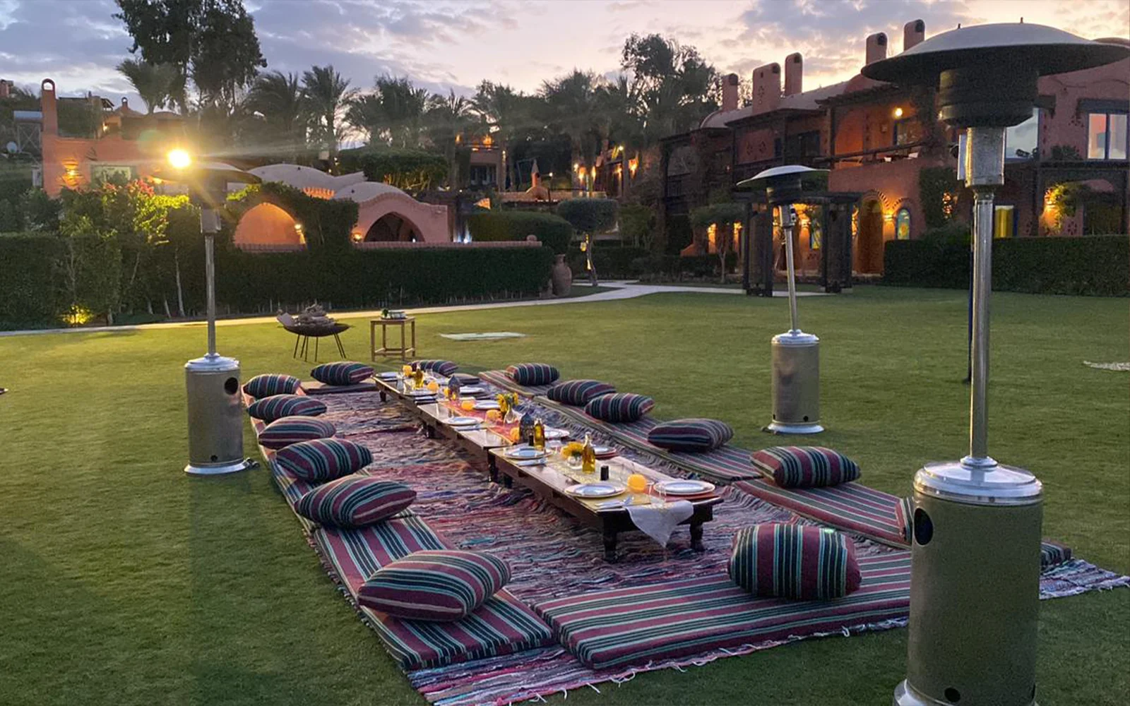 Low floor-seating dinner laid out on rugs on a lawn at dusk.
